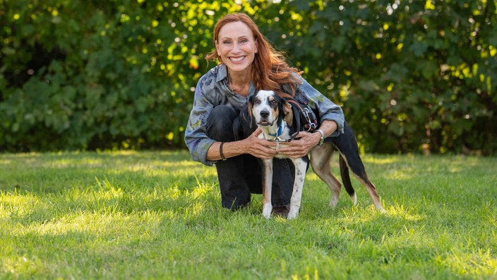 Schauspielerin Andrea Sawatzki mit einem dreifarbigem Hund auf einer Wiese 