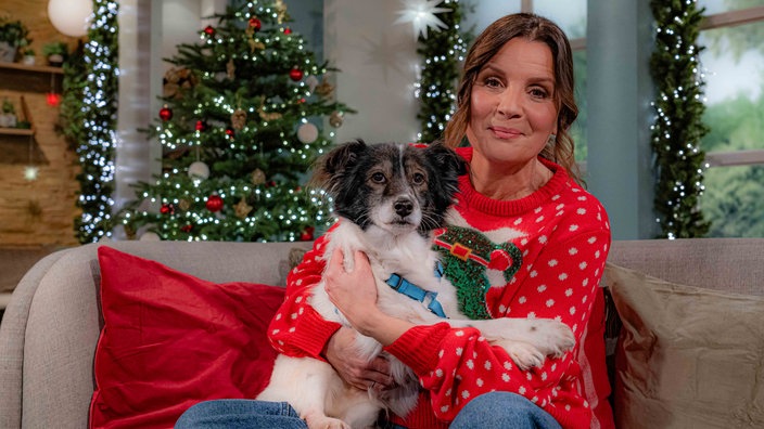 Moderatorin Simone Sombecki sitzt im Studio mit einem Hund auf dem Schoß auf einem Sofa 