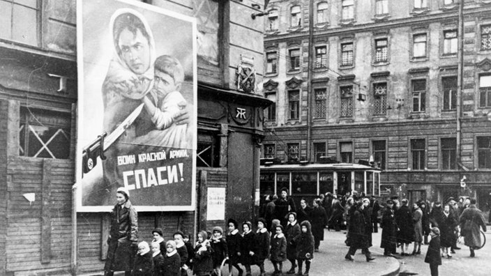 Eine Kindergruppe läuft vor einem Plakat entlang, das zur Verteidigung der sowjetischen Heimat aufruft, aufgenommen 1942