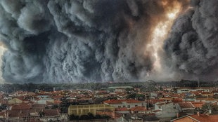 Blick auf eine Stadt, im Hintergrund eine Feuer- und Rauchwalze