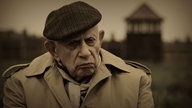 Henryk Schoenker, nah, im Hintergrund das Eingangsgebäude von Auschwitz-Birkenau 