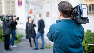 Eine Reporterin interviewt einen Mann, Kameraleute filmen die Situation.