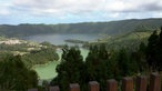 Blick über Nadelbäume auf Landschaft mit zwei Seen, der eine leuchtet grün, der andere blau