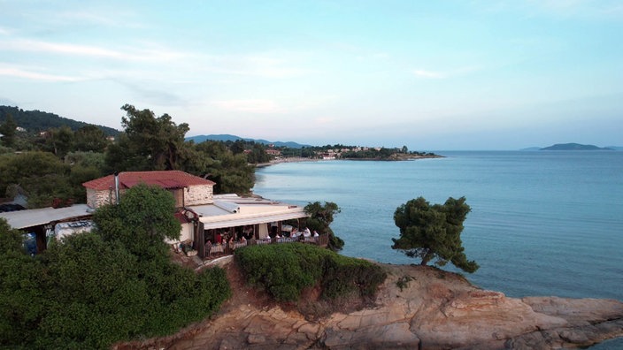 Blick auf Bucht im Sonnenuntergang, im Vordergrund ein Restaurant mit Terrasse