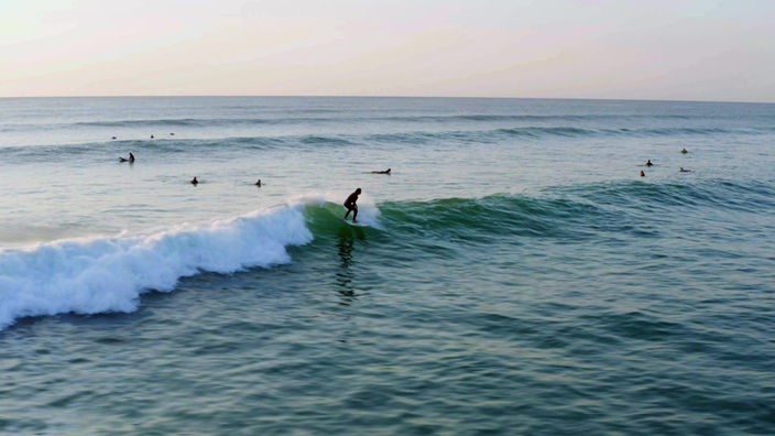Mehrere Surfer und Schwimmer im wellenbewegten Meer