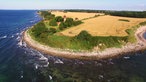 Blick auf ein Kap mit Kiesstrand, Feldern und einem Leuchtturm