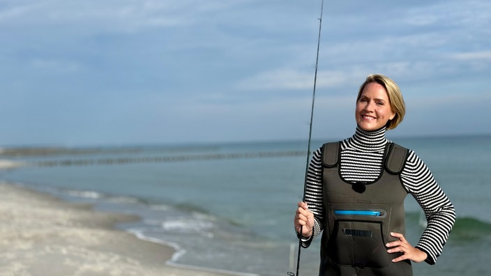 Judith Rakers steht mit der Angel in der Hand am Strand