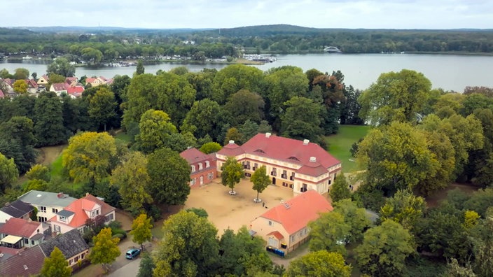 Blick auf Schloss Caputh umgeben von Bäumen, im Hintergrund die Havel