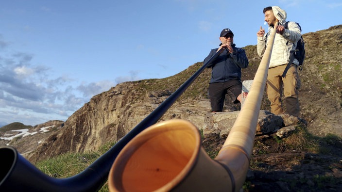 Ramon Babazadeh (r) und der Wanderführer stehen jeweils mit einem Alphorn auf dem Berg