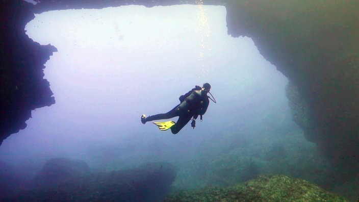 Taucher in einer bläulich erstrahlenden Unterwassergrotte