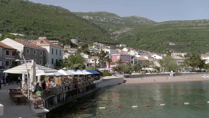 Kleiner Ort an der Küste mit Strand, dahinter bewaldete Berge