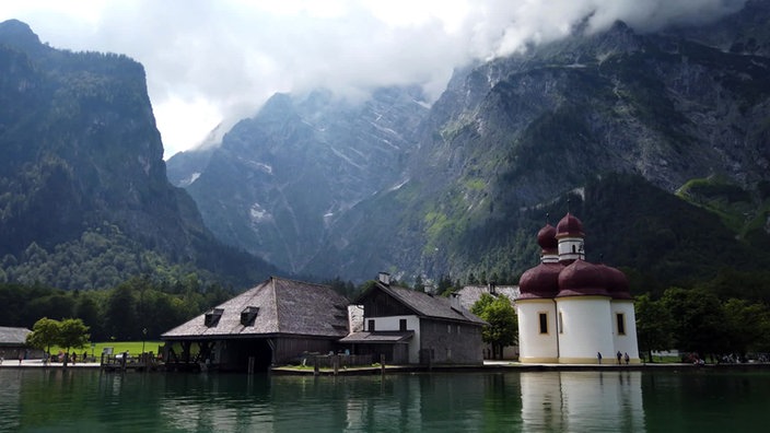 Kleine Kapelle und weiteres Gebäude am Seeufer vor steilen Felswänden