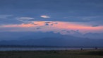 Ebene Landschaft mit zwei Elefanten, dahinter ein See und Berge, darüber Sonnenuntergang mit Wolken