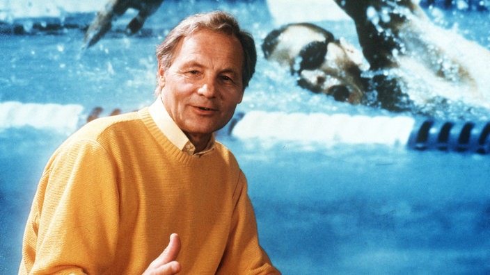 Harry Valérien 1984 in gelbem Pulli bei Anmoderation vor Standbild Schwimmwettbewerb 