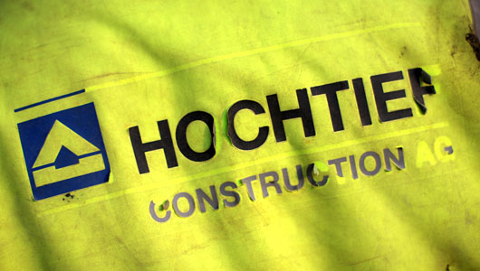 Der Schriftzug "Hochtief" blättert von einer Regenjacke ab