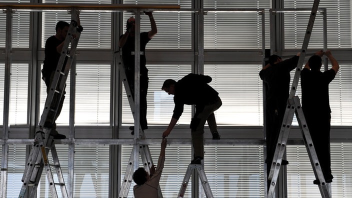 Arbeiter stehen auf einem Gerüst vor Jalousien