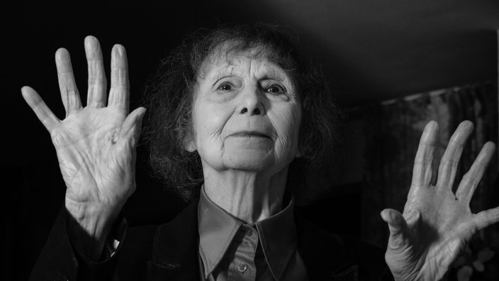 Schwarzweißaufnahme: Sofia Gubaidulina gestikultiert mit beiden Händen.