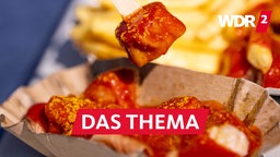 Eine Person spießt ein Stück Currywurst aus einer Schale auf.