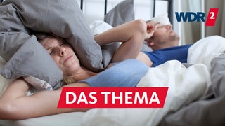 Eine Frau liegt neben ihrem schnarchenden Partner im Bett und hält sich die Ohren zu