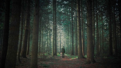 Eine Person läuft alleine durch einen dunklen Wald.