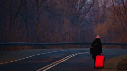 Eine Frau, die vor dem Krieg in der Ukraine geflohen ist, geht mit ihrem Gepäck an der ukrainisch-polnischen Grenze in Kroscienko.