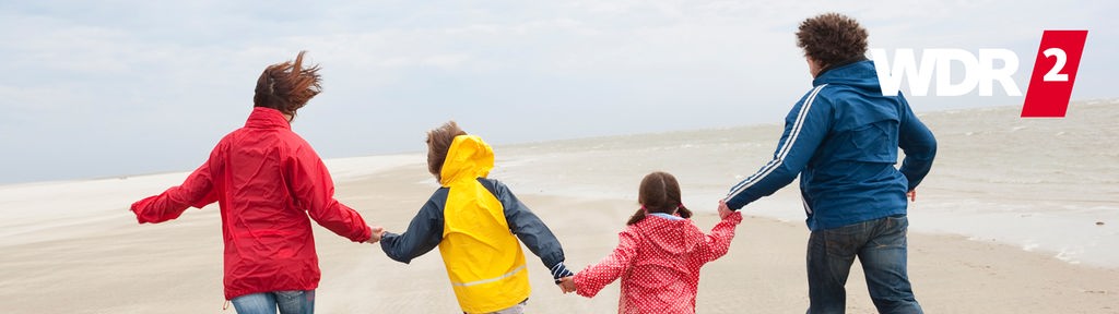 Zwei Erwachsene und zwei Kinder laufen an einem Nordseestrand