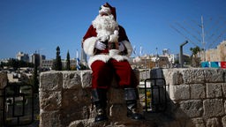 Issa Kassissieh sitzt als Weihnachtsmann verkleidet auf einer Mauer in Jerusalem.