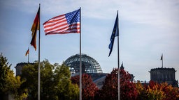 Die Flaggen Deutschlands, der USA und der EU wehen im Wind, im Hintergrund der Reichstag in Berlin. 