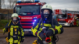 Zwei Feuerwehrleute vor Löschfahrzeugen