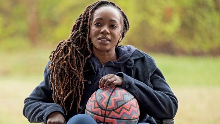 Eine Frau im Rollstuhl mit einem Basketball in den Händen.