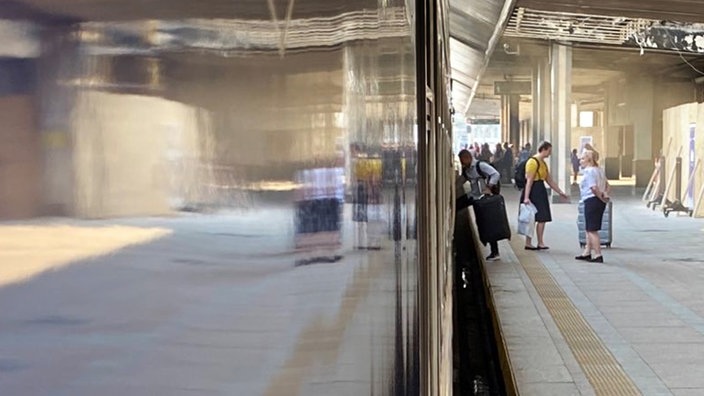 Menschen in der Ferne, die aus einem Zug am Bahnhof ein- und aussteigen.