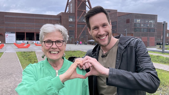 Sven Kroll und Gerburg Jahnke machen mit ihren Händen ein Herz vorm Zeche Zollverein in Essen.