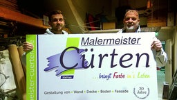 Zwei Männer halten ein Schild eines Malermeisterbetriebs