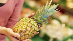 Eine Frau nimmt sich eine Ananas im Supermarkt.