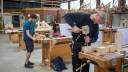 Zwei Azubis stehen an einer Werkbank und bearbeiten Holz