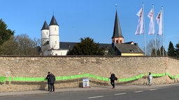 Grüne Zettel an der Steinmauer vor dem Kloster mit der Aufschrift "Übernehmt Verantwortung für die Verbrechen"