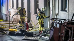 Feuerwehrleute arbeiten im Eingangsbereich eines Mehrfamilienhauses.