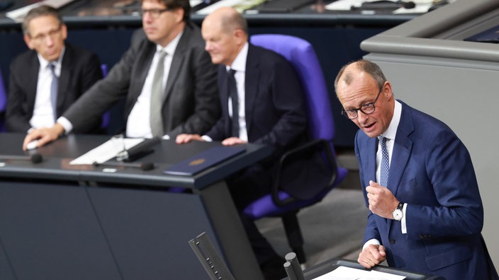 CDU-Chef Friedrich Merz steht am Rednerpult im Bundestag. Im Hintergrund Bundeskanzler Olaf Scholz.