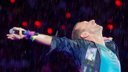 Chris Martin, Sänger der britischen Band Coldplay steht bei einem Konzert im Rahmen der "Music of the Spheres Tour 2024" bei strömendem Regen in der Merkur auf der Bühne. 