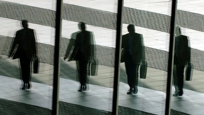  Ein Mann mit Aktentasche geht in Bonn ins Büro und spiegelt sich dabei in den Glasscheiben des Post-Towers