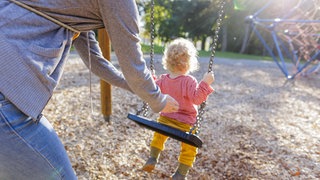 Kind auf Schaukel wird von Mutter angeschubst