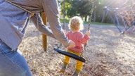 Kind auf Schaukel wird von Mutter angeschubst