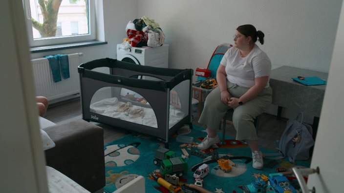 Sozialarbeiterin Sophie Schöttler sitzt bei einem Hausbesuch in einem Kinderzimmer mit Spielteppich und Kinderbett