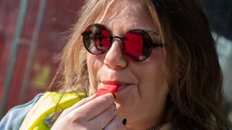 Eine Frau mit Sonnenbrille und Warnweste pustet in eine Pfeife