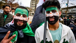 Zwei junge Männer haben sich für eine Kundgebung in Wuppertal eine syrische Flagge ins Gesicht gemalt.