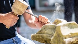 Ein Restaurator, bearbeitet ein Stück der Ruine am Romberger Hof mit einem Meißel und Holzhammer.