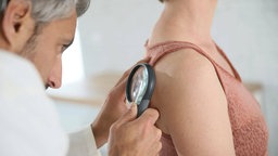 Dermatologe untersucht Patientin mit einer Lupe