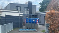 An einem Einfamilienhaus in Köln-Rodenkirchen sind Spuren des SEK-Einsatzes vom Juli noch sichtbar. Ein Container steht in der Einfahrt, der beschädigte Treppenabsatz wird repariert.