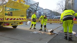 Drei Müllwerker beladen mit Besen und Schaufel den Müllwagen, nachdem während des Streiks der Müll liegengeblieben war