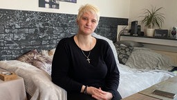 Frau mit kurzen blonden Haaren  sitzt auf dem Sofa in ihrem Wohnzimmer. 